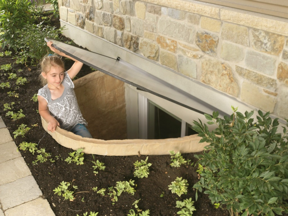 a young girl lifts an egress window well cover to safely escape basement