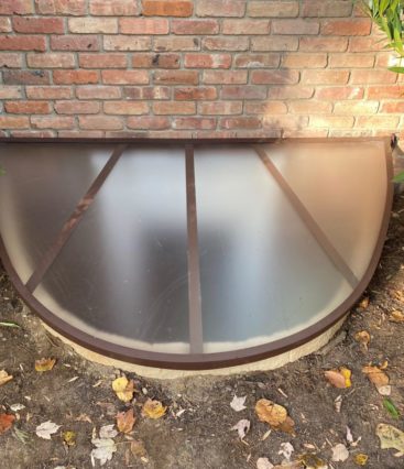 egress window well cover surrounded by fallen leaves