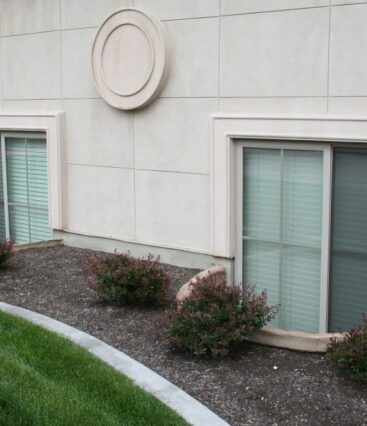 two egress windows with window wells surrounded by mulching and plants egress solutions landscaping around window wells